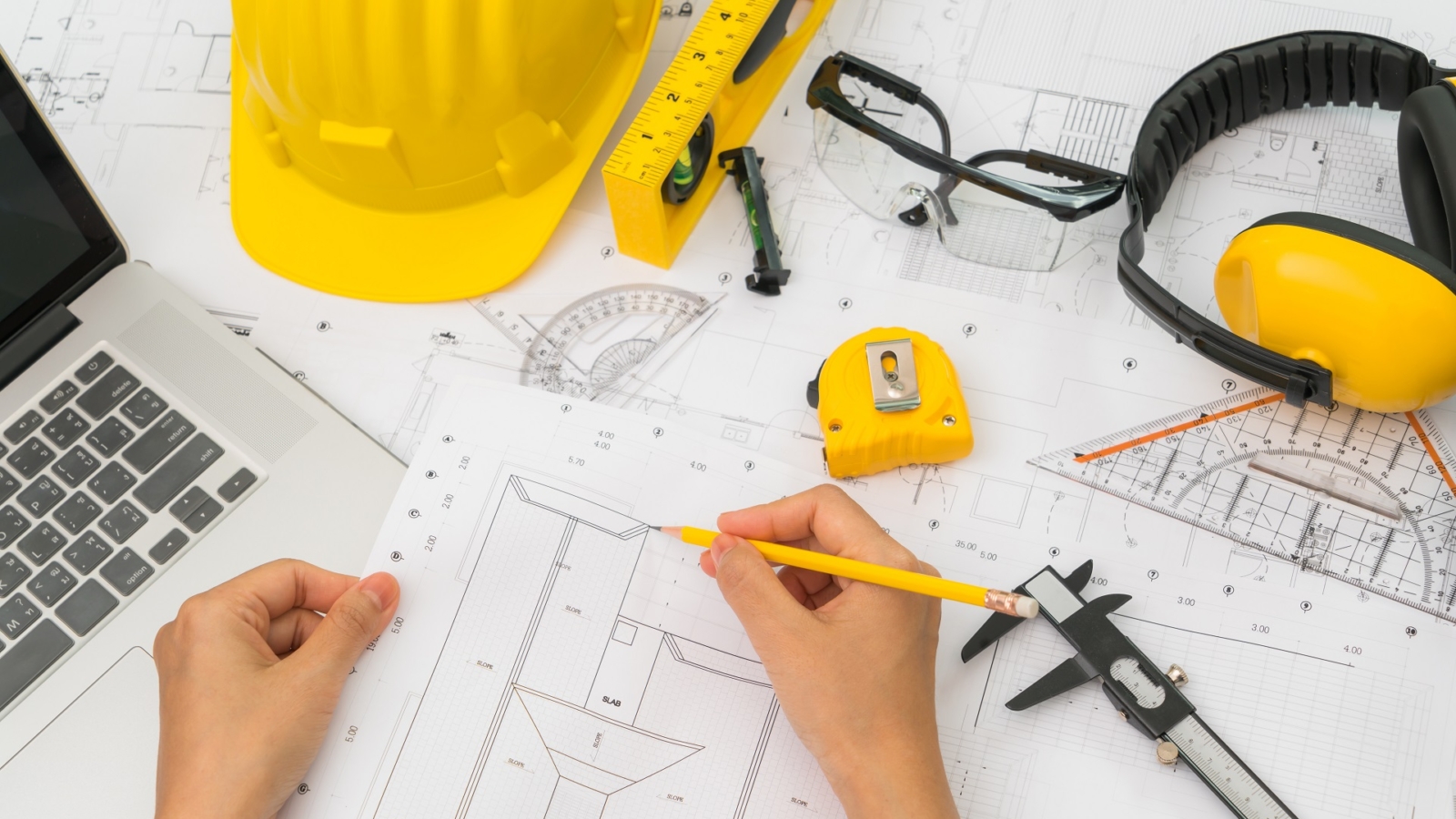 Hand over Construction plans with yellow helmet and drawing tools on blueprints