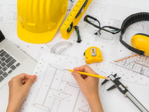 Hand over Construction plans with yellow helmet and drawing tools on blueprints